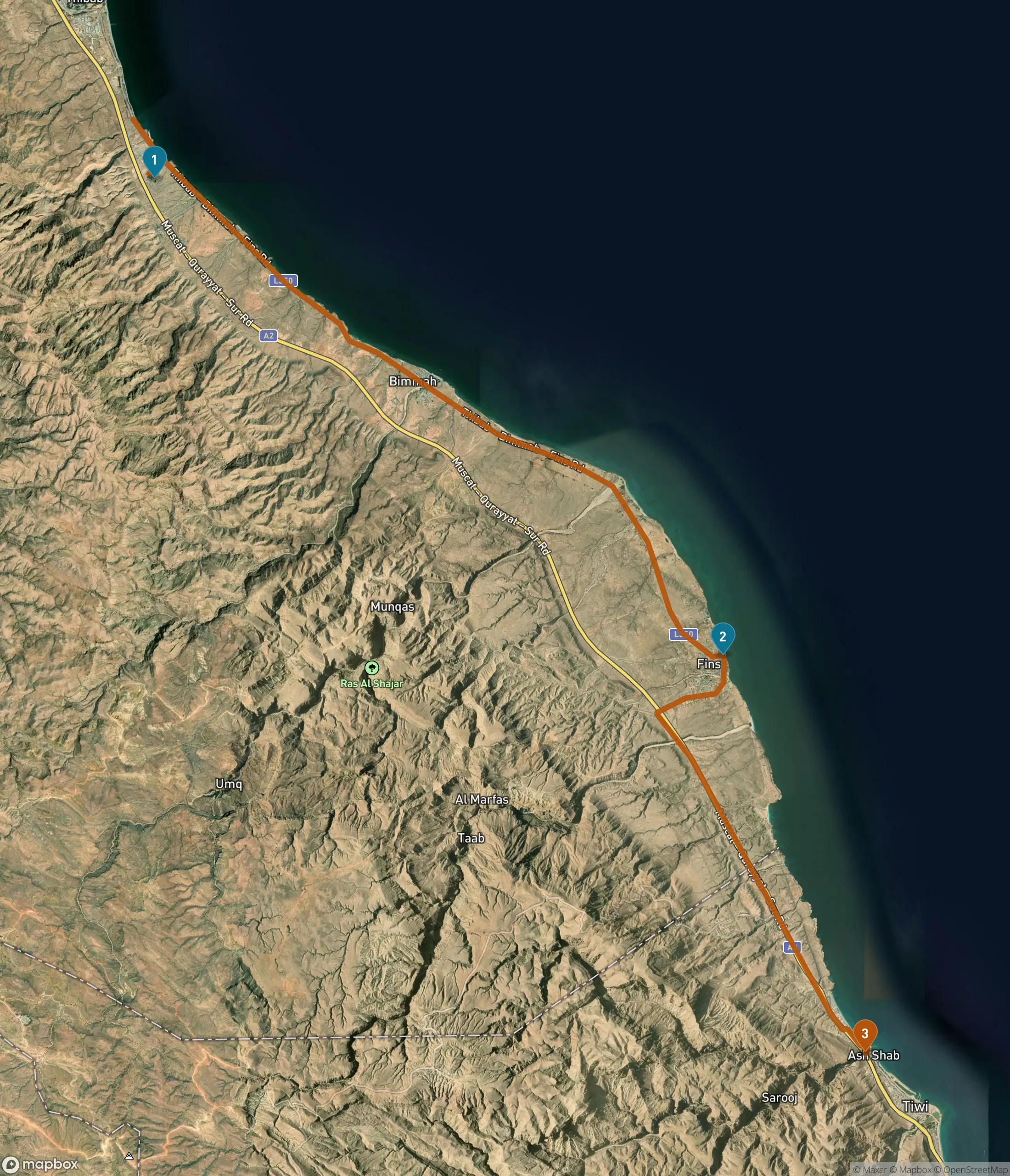 Satellite map of a 33-kilometre stretch of the Oman coast between bare mountains and the sea. An orange road line runs from Bimmah Sinkhole, marked 1, south past Fins Beach, marked 2, to the Wadi Shab parking area near Tiwi, marked 3. The Muscat to Qurayyat to Sur road is labelled along the shoreline.