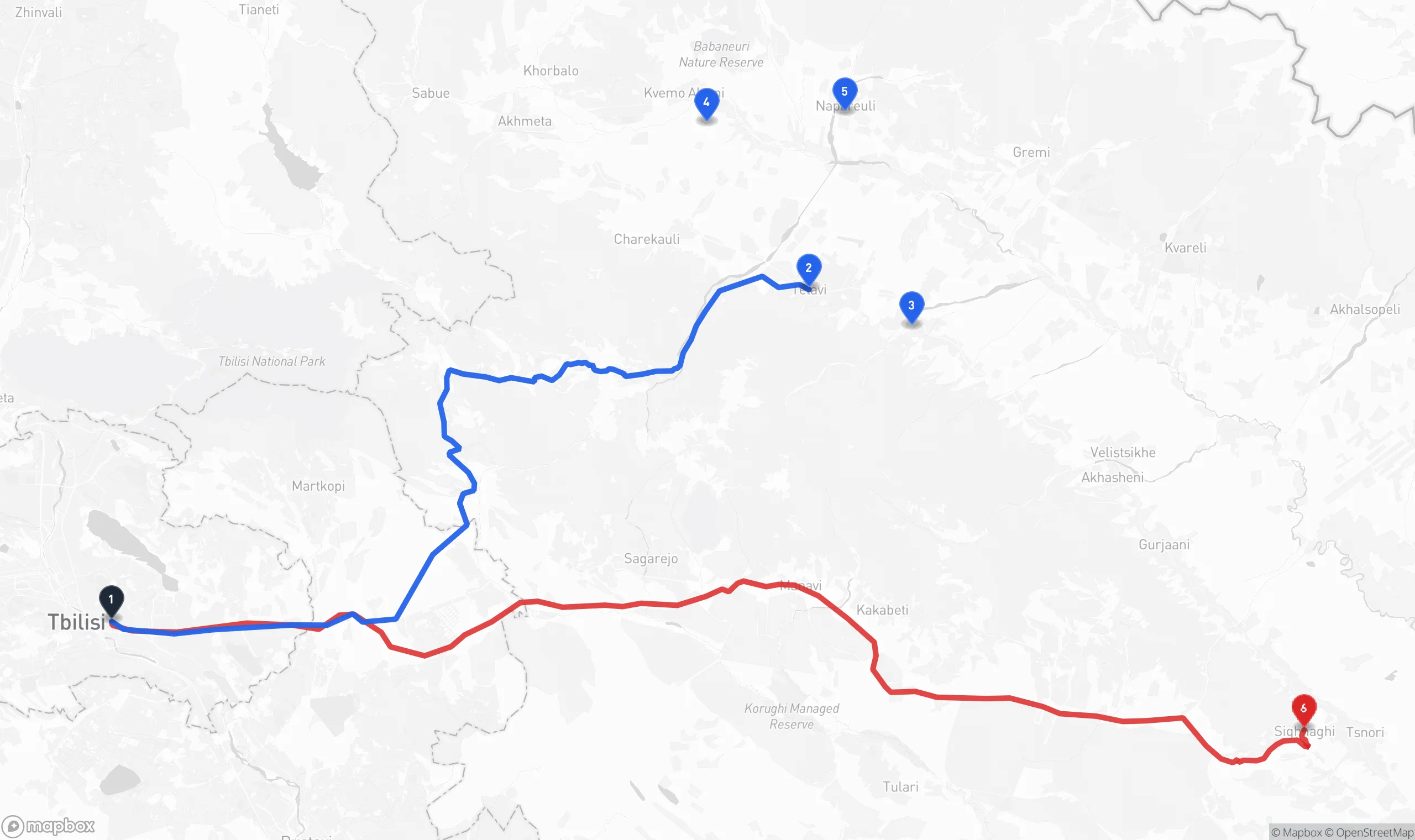 Map of eastern Georgia showing Tbilisi at lower left and two driving routes into the Kakheti wine region: a blue route north over the Gombori Pass to Telavi with the Tsinandali, Alaverdi and Napareuli winery cluster around it, and a longer red route running southeast through Sagarejo and Gurjaani to the hilltop town of Sighnaghi.