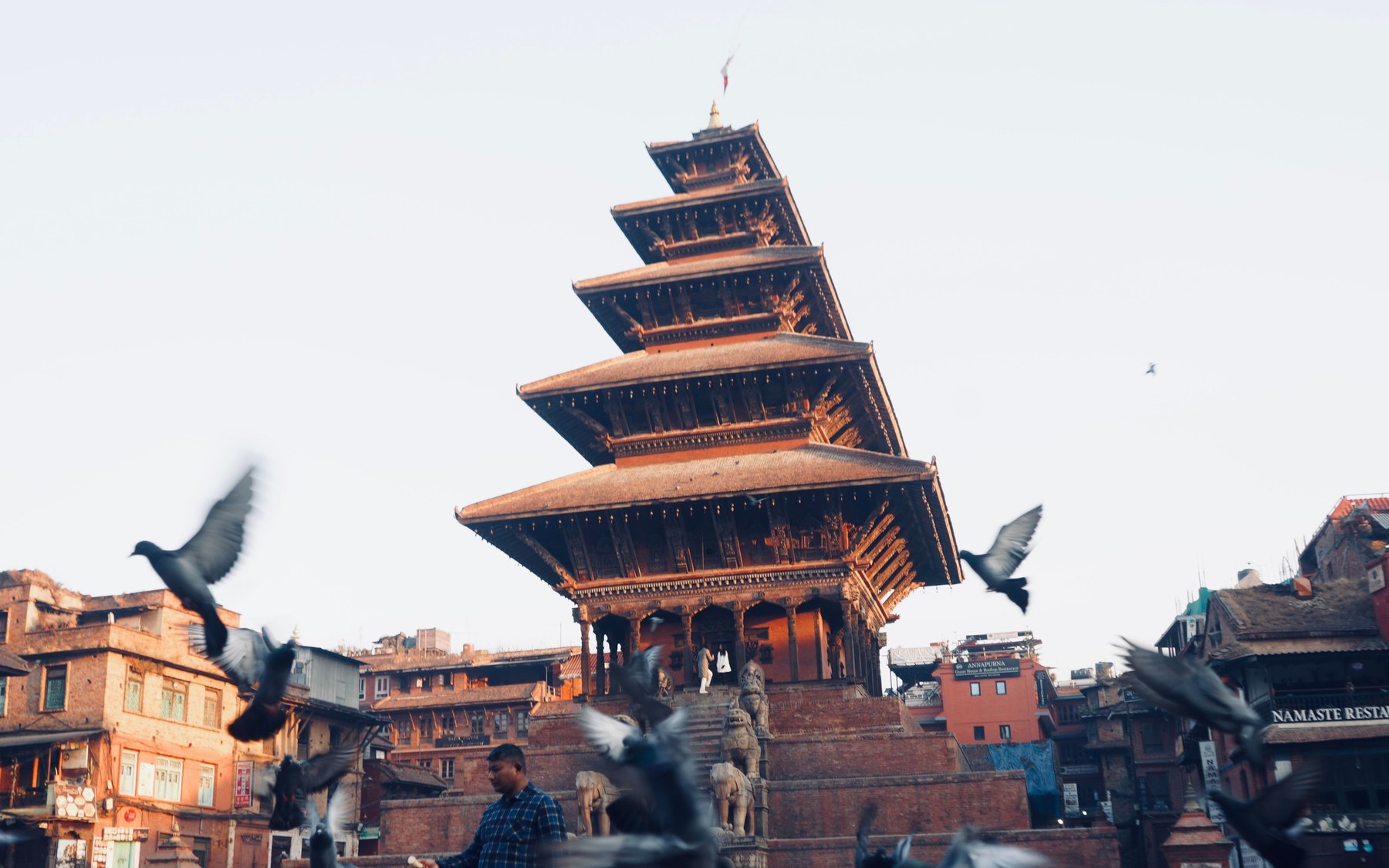 The five-tiered Nyatapola Temple rising over Taumadhi Square in Bhaktapur at first light, with pigeons scattering across the empty brick square below.