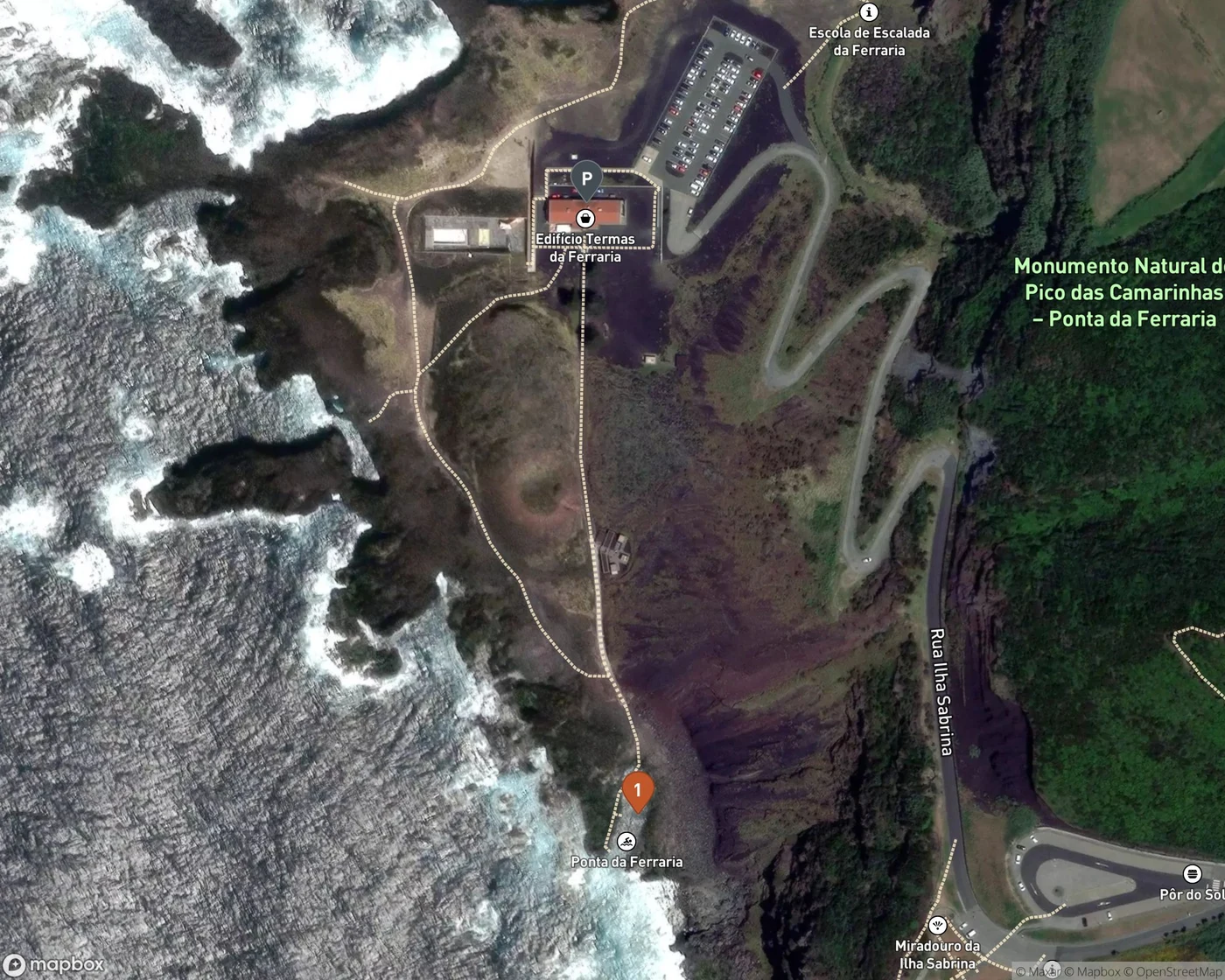 Satellite map of the western tip of São Miguel at Ponta da Ferraria, showing the clifftop car park and the Edifício Termas da Ferraria building marked P, a paved track running south down the headland, and pin 1 at the natural sea pool on the black lava point below, with the Atlantic breaking white against the rocks and a hairpin access road climbing inland to the east.
