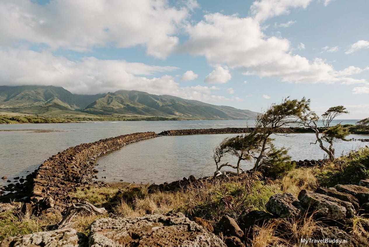 A quiet Molokaʻi fishpond coastline with calm water, low mountains, and trade-wind clouds.