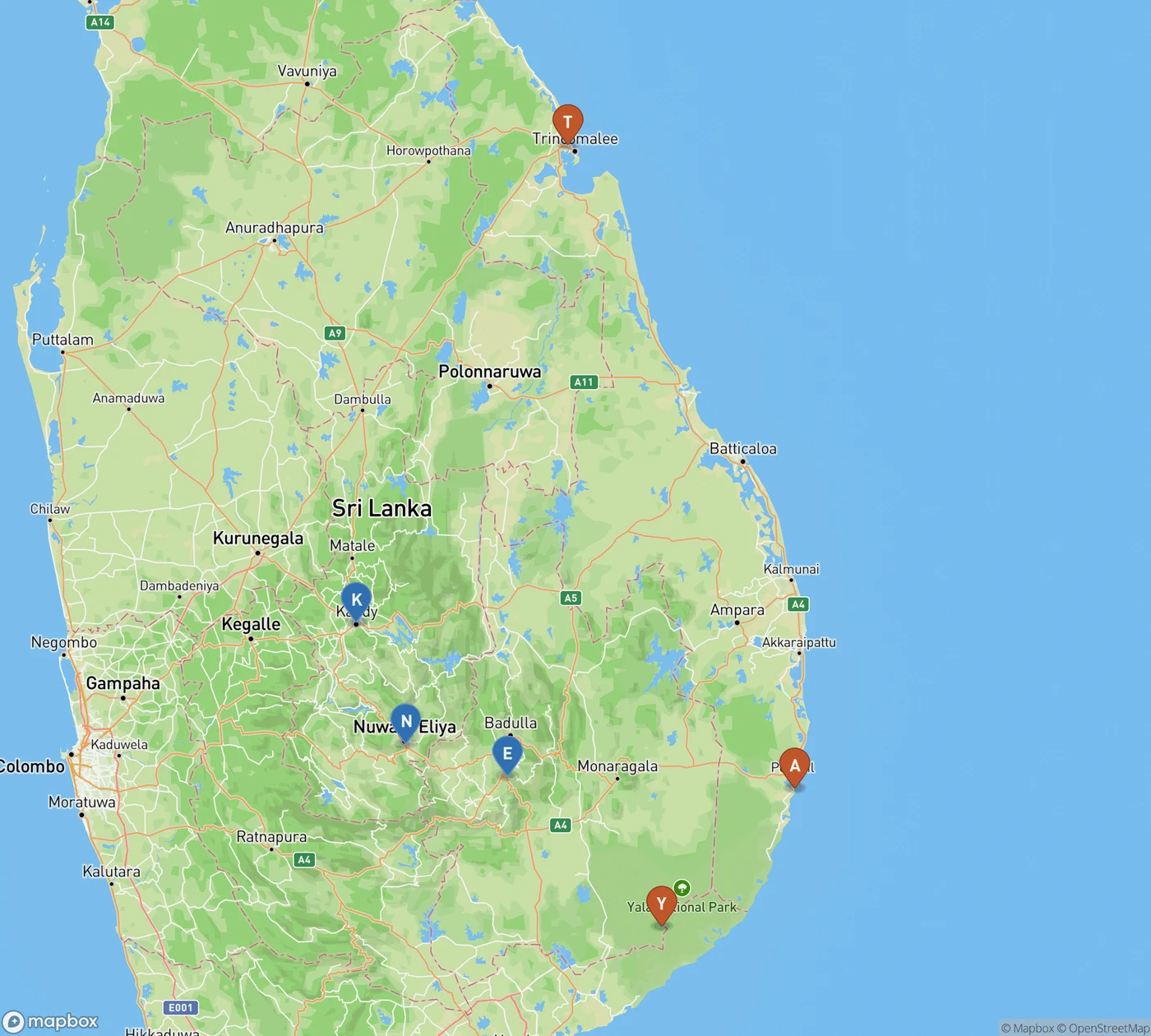 Map of Sri Lanka comparing forecast rainfall. Blue pins mark the hill country — K for Kandy, N for Nuwara Eliya and E for Ella — running down the centre and south of the island, the wettest band in the 8 to 23 October forecast. Orange pins mark the drier southeast and east: T for Trincomalee on the northeast coast, A for Arugam Bay on the east coast and Y for Yala National Park in the far southeast.